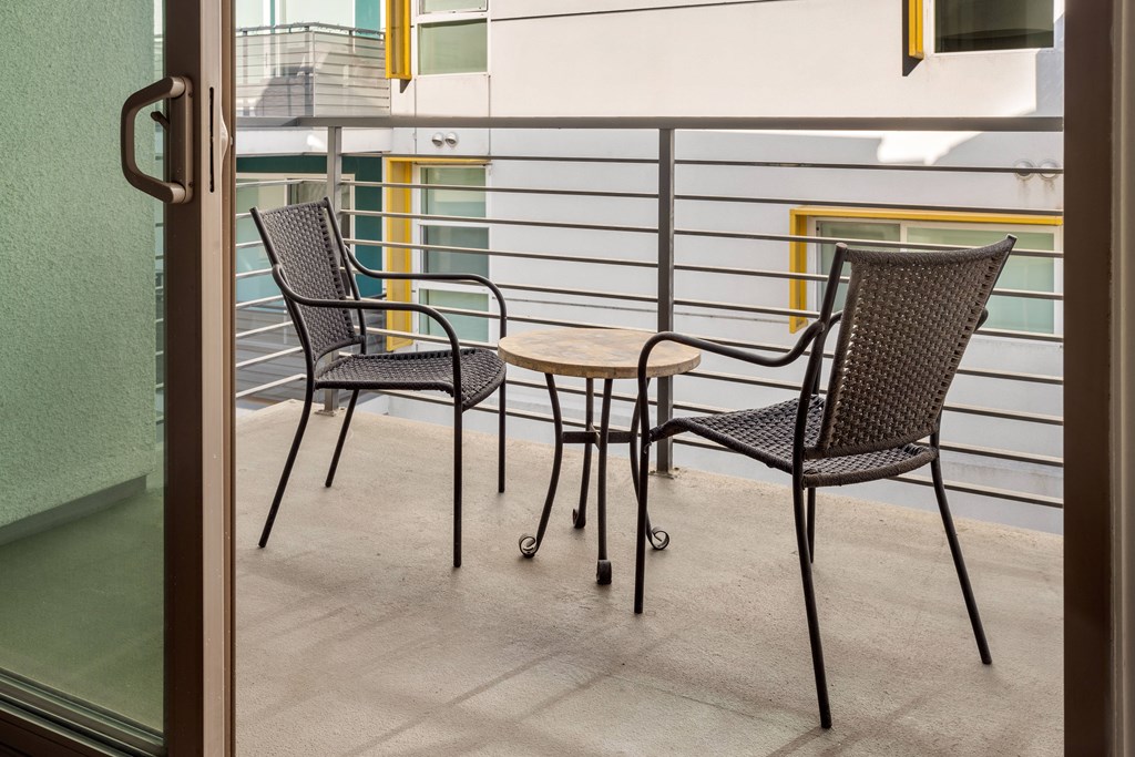 Two chairs and a table are on a balcony.