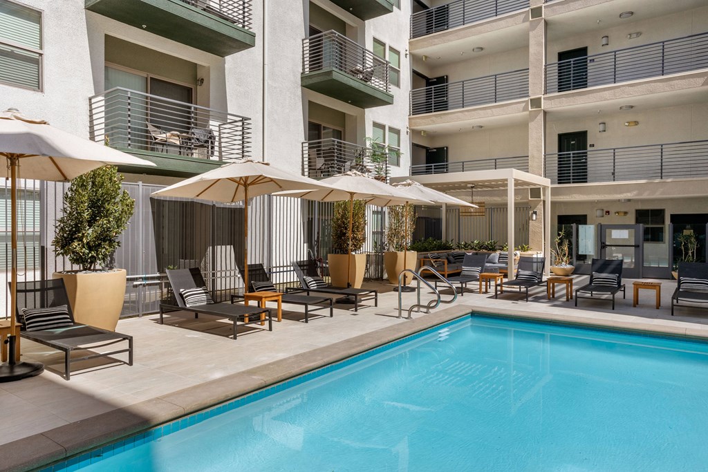 A pool area with chairs and umbrellas in front of a building.