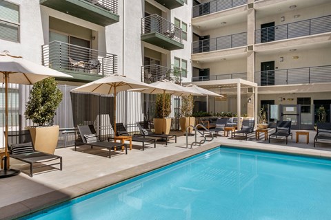 A pool area with chairs and umbrellas in front of a building.