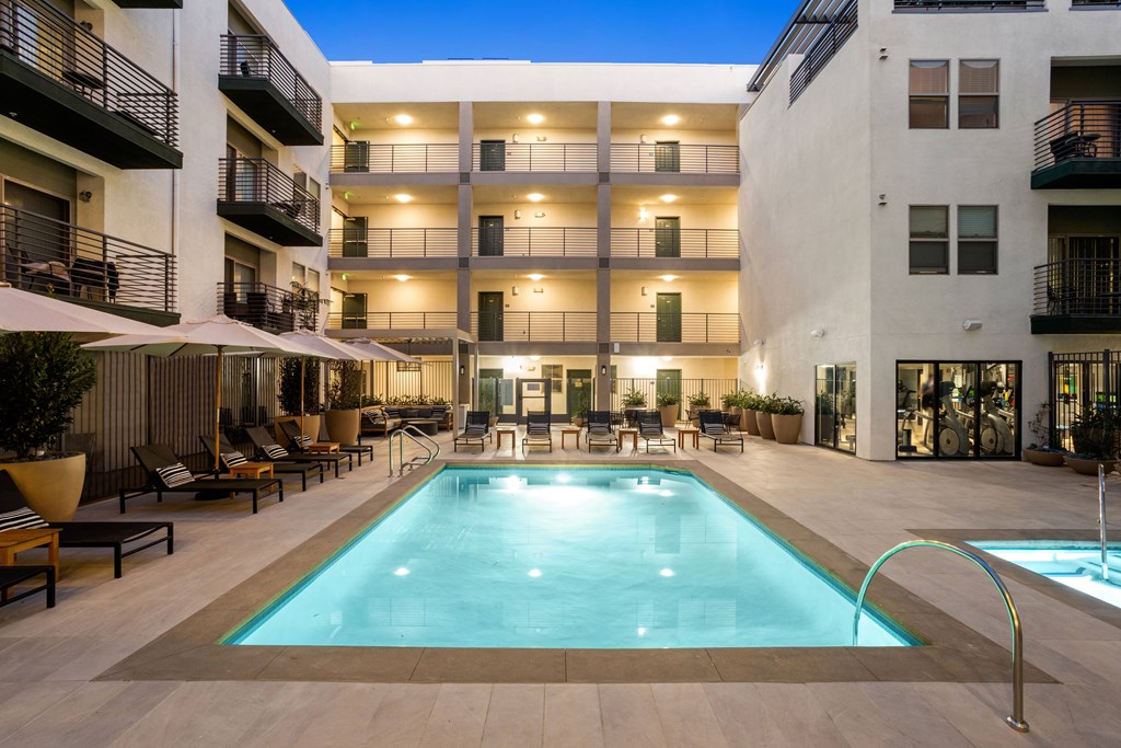 A large swimming pool in the middle of a courtyard surrounded by lounge chairs and umbrellas.