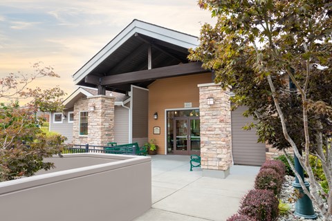 A building with a brown facade and a stone pillar is surrounded by greenery.