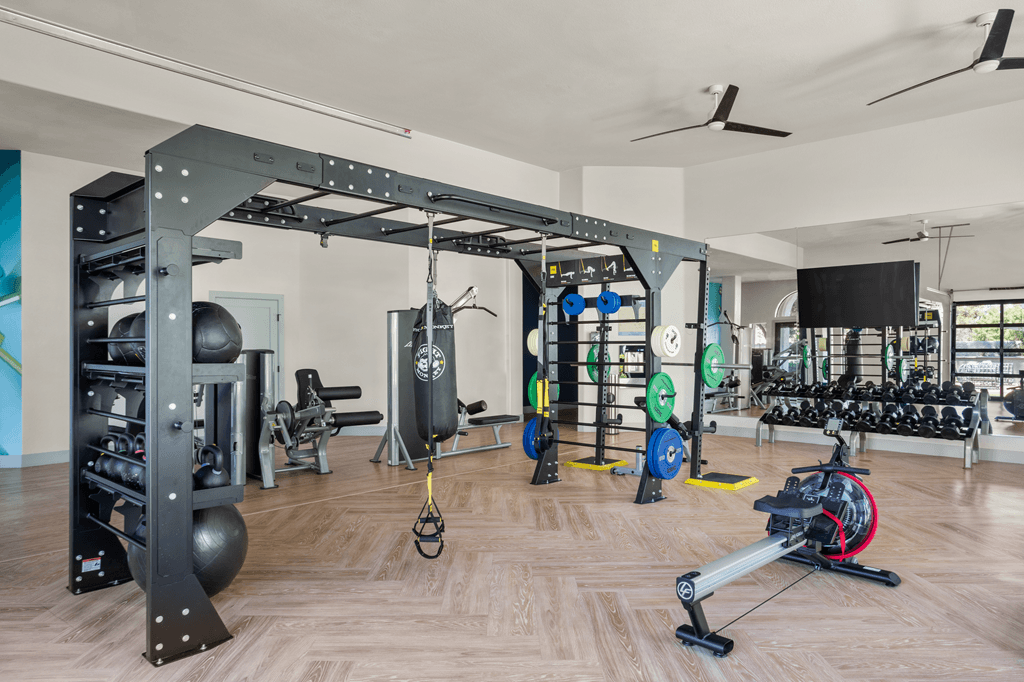 A gym with a variety of equipment including a weight bench, barbell, and a rowing machine.