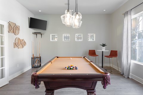 A pool table is in the middle of a room with a TV and a chair.