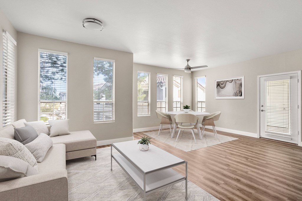 A living room with a white couch, a glass coffee table, and a dining table with chairs.