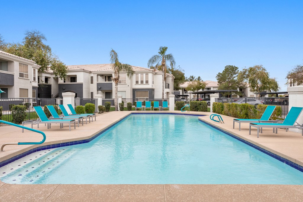 A large swimming pool with lounge chairs and a building in the background.