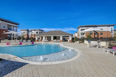 A large outdoor swimming pool surrounded by a brick patio and lounge chairs.