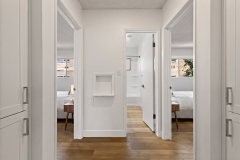 A white hallway with a bedroom and a bathroom visible through the door.