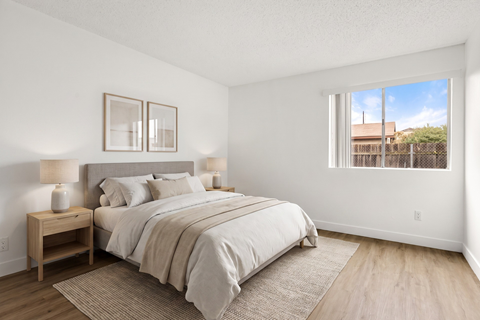 A bedroom with a large bed and a window overlooking a fence.