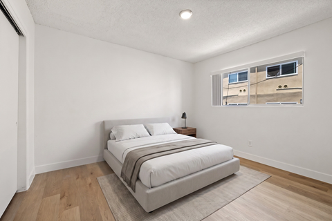 A bedroom with a large bed and a window showing a building outside.