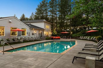A swimming pool surrounded by lounge chairs and umbrellas outside a house.