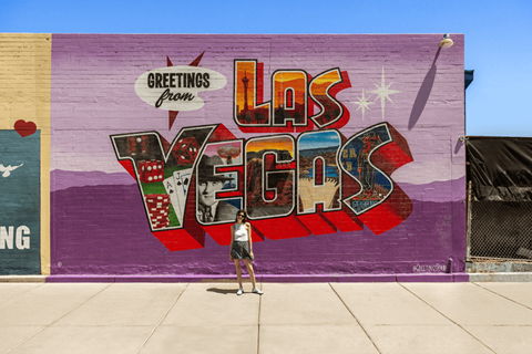 A person stands in front of a mural that says "Greetings from Las Vegas".