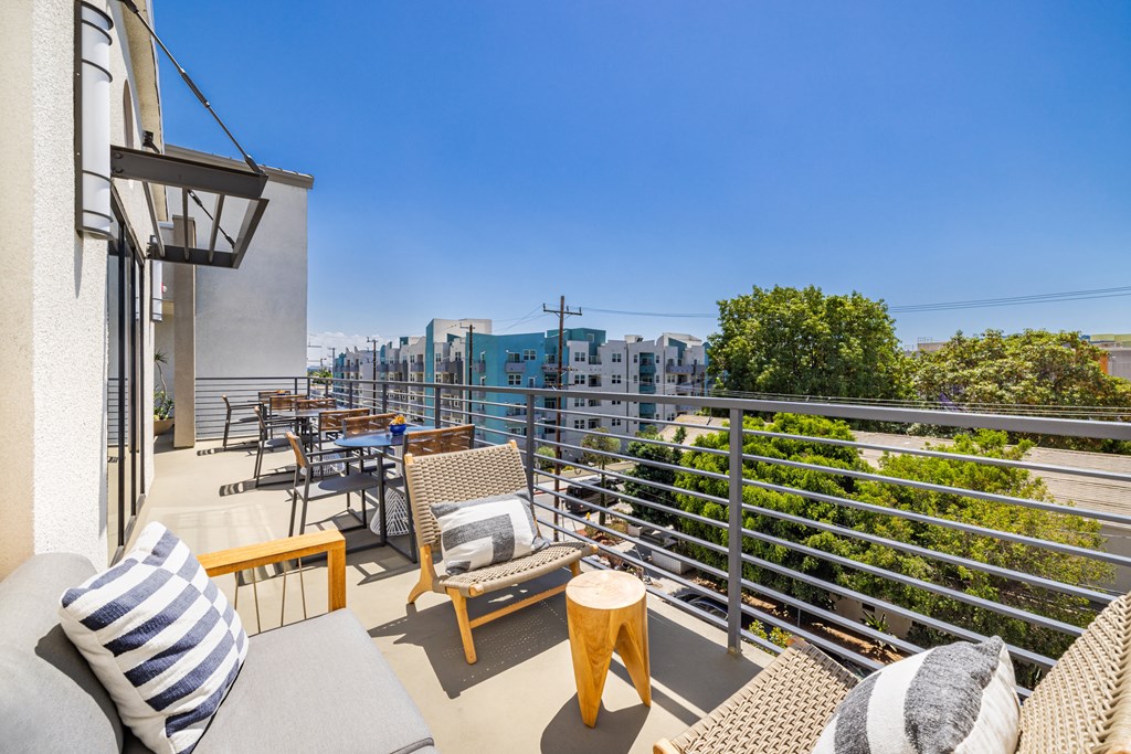 A balcony with a grey couch, wooden chairs and a table with a striped pillow.