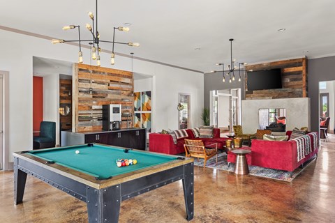 A pool table is in the middle of a room with a red couch and a TV.