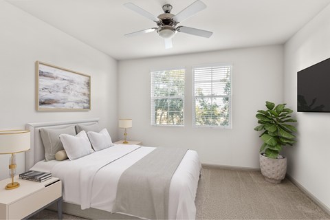 A bedroom with a bed, a ceiling fan, a nightstand with a lamp, a potted plant, and a painting on the wall.