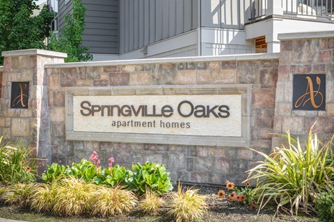 A sign for Springville Oaks apartment homes is displayed in front of a building.