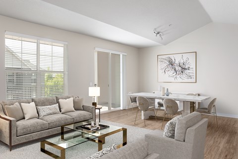 A modern living room with a grey sofa, a glass coffee table, and a dining table set up.