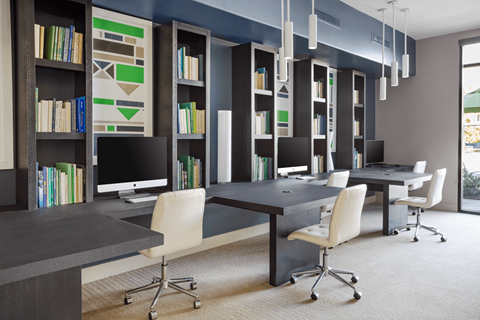 A modern office with a long table and chairs, a computer on the table, and a bookshelf with books and decorative items.