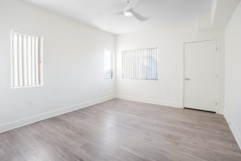 A room with a ceiling fan and light, hardwood floors, and two windows with blinds.