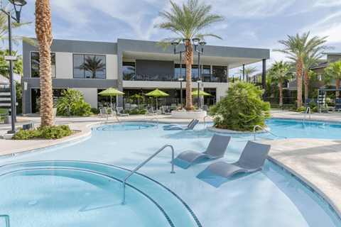 A swimming pool with lounge chairs and palm trees in front of a modern building.