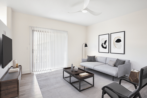 A living room with a grey couch, a black chair, a coffee table, and a flat screen TV mounted on the wall.