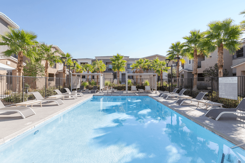 A swimming pool surrounded by lounge chairs and palm trees.