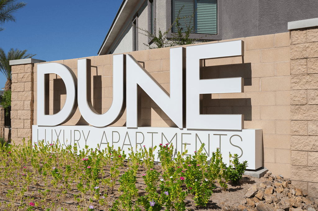 A sign for Dune Luxury Apartments is displayed in front of a building.