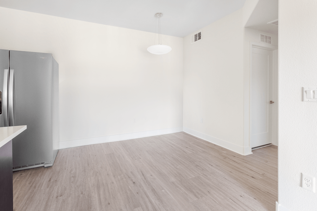 A kitchen with a refrigerator and a wooden floor.