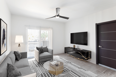 A living room with a grey couch, a coffee table, a flat screen TV, and a ceiling fan.