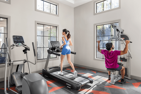 A woman is running on a treadmill while a man is working out on a cable machine in a gym.