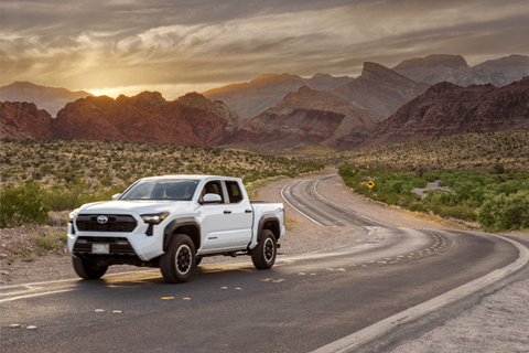 A white Toyota truck is driving on a winding road in a desert landscape.