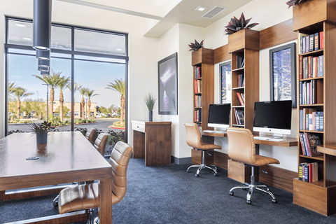 A room with a desk, chairs, and a bookshelf with a view of palm trees outside the window.