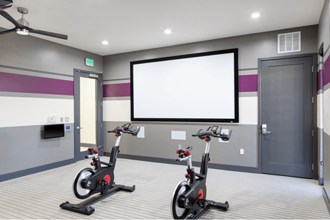 Two stationary bikes are in a room with a white screen.