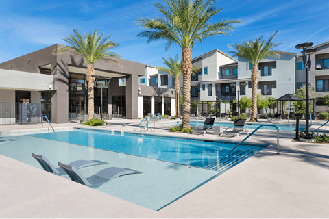 A swimming pool surrounded by palm trees and lounge chairs in front of a modern building.