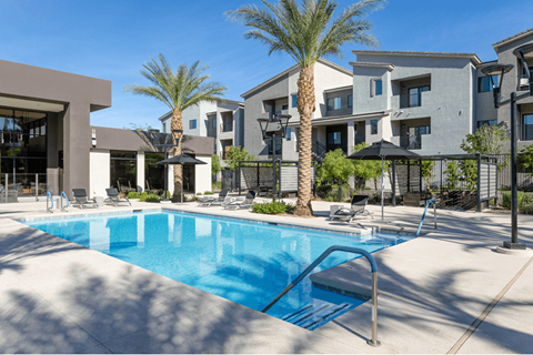 A swimming pool surrounded by palm trees and lounge chairs in front of apartment buildings.