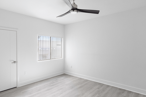 A room with a ceiling fan and a window with bars.