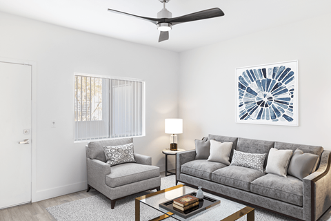 A living room with a grey couch, a grey armchair, a coffee table, a ceiling fan, and a painting on the wall.