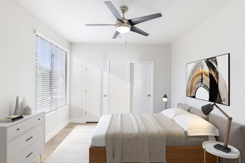 A bedroom with a bed, a ceiling fan, and a painting on the wall.
