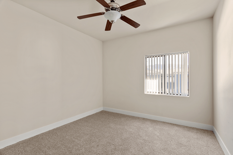 A room with a ceiling fan and a window with blinds.
