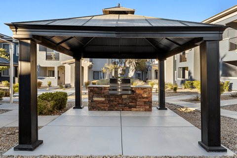 A gazebo with a stone fireplace is in the middle of a courtyard.