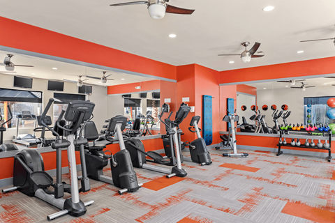 A gym with orange walls and a variety of exercise equipment.