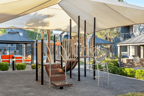 A playground with a slide and a climbing frame under a large shade structure.