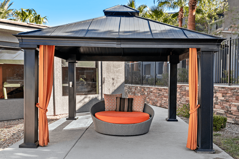 A black gazebo with orange curtains and a grey couch.