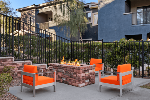 Two orange chairs are placed in front of a fire pit.