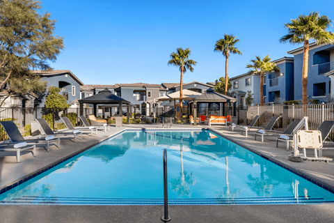 A swimming pool surrounded by lounge chairs and palm trees.