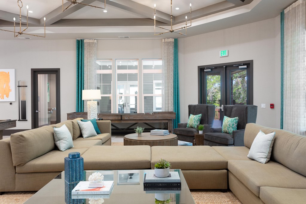 A well-lit, modern living room with a large sectional sofa, a coffee table, and a view of the outdoors through a large window.
