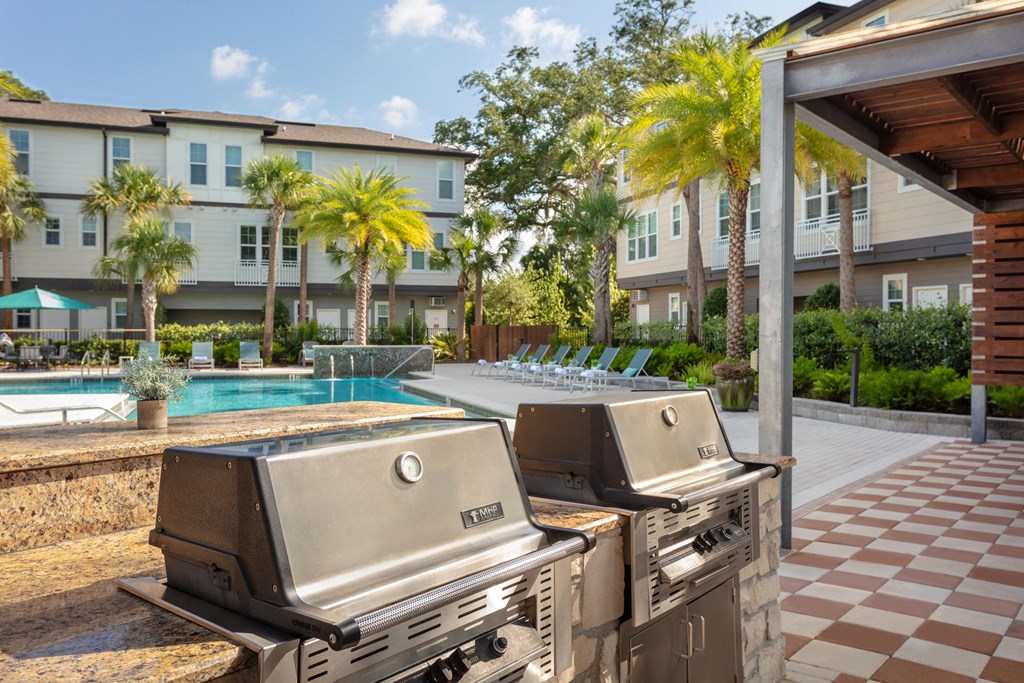 Two grills are in the foreground of a resort with a pool and palm trees.