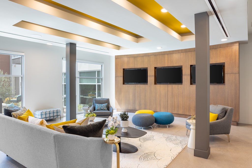A modern living room with a grey sofa, yellow and blue cushions, a wooden cabinet, and a large window.