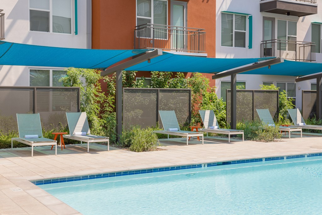 A pool with a blue canopy and lounge chairs.