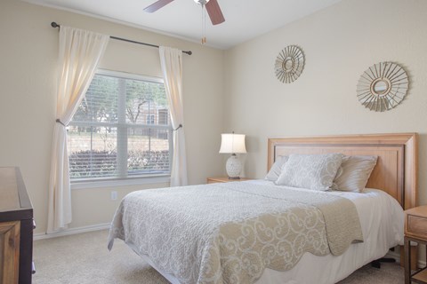A bedroom with a bed, nightstand, and window with curtains.