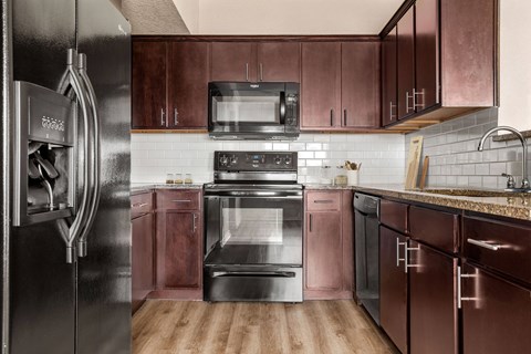 A kitchen with a black refrigerator and brown cabinets.